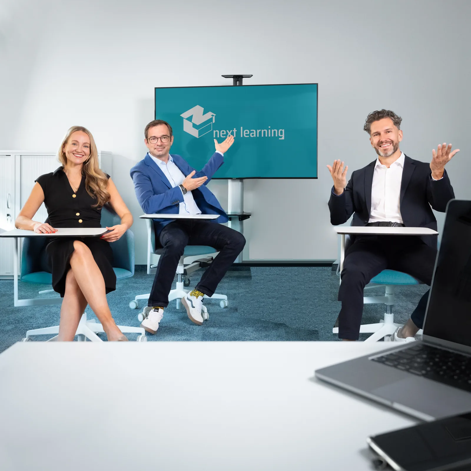 Das Team der next learning im Halbkreis vor dem Bildschirm mit dem Logo der Gesellschaft